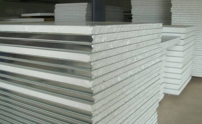 Close-up of stacked EPS panels showing white foam edges between steel sheets, more stacks behind