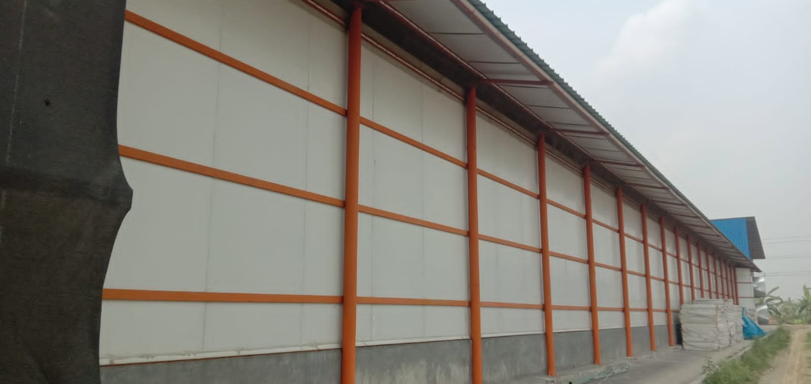 Long shed wall of white panels held by orange steel battens