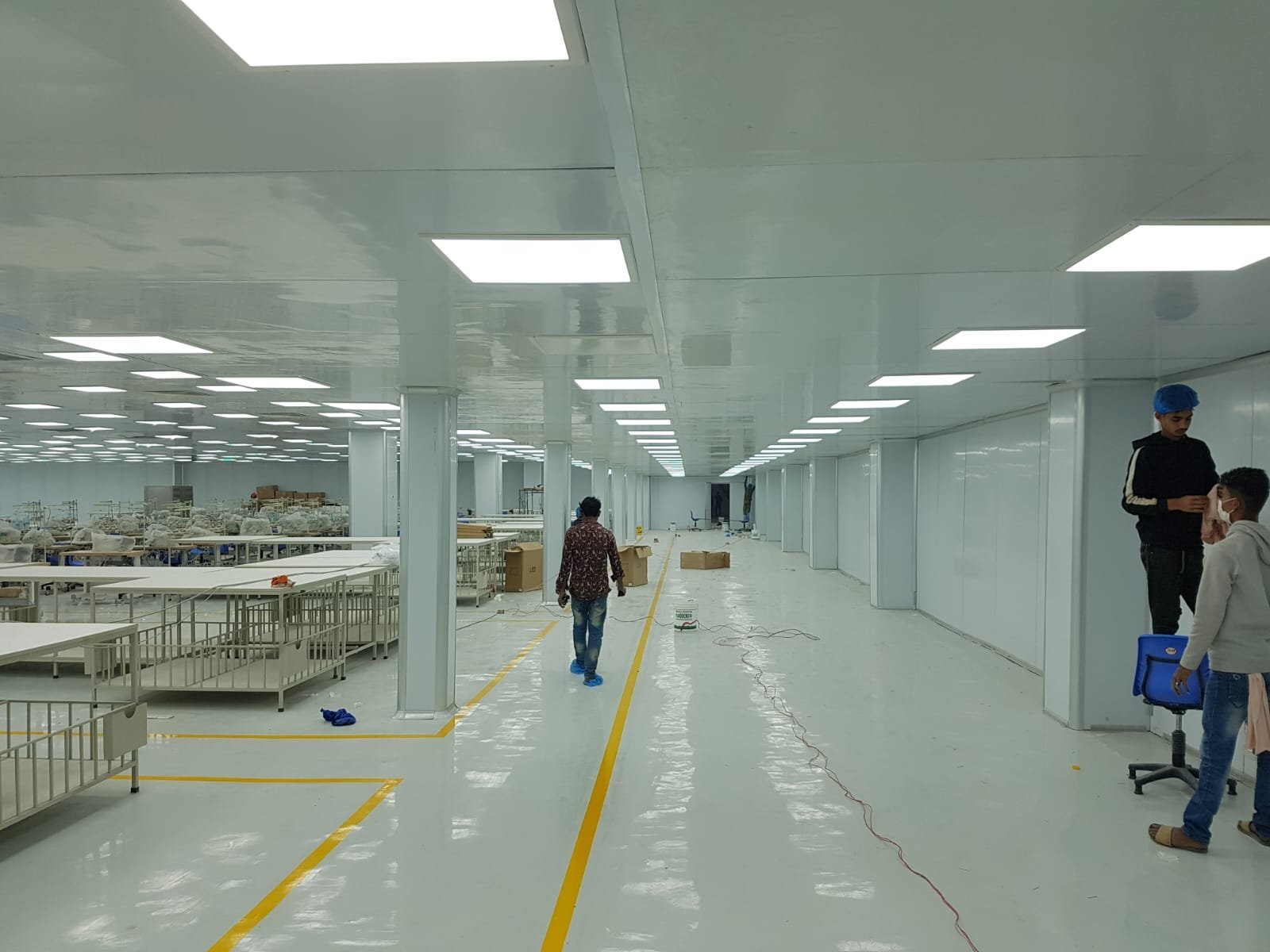 Factory hall lined with white insulated wall and ceiling panels, workers and work tables